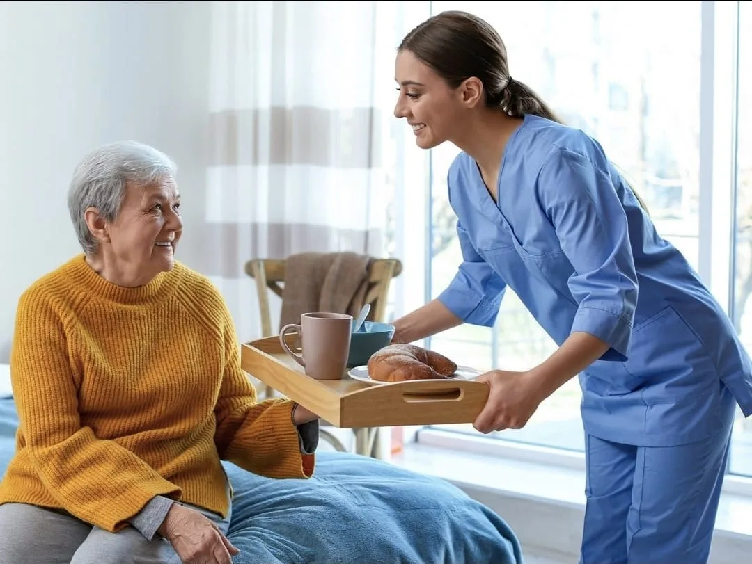 Une aidante apporte un repas à une personne âgée